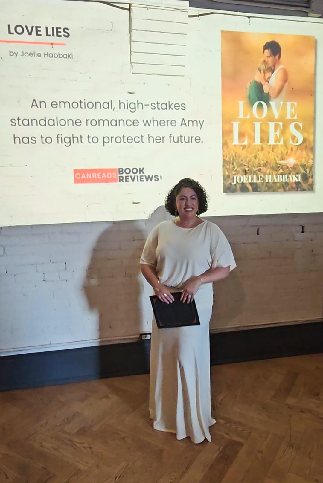 Joelle Habbaki holding her novel Love Lies beside a 2026 CANREADS Finalist graphic